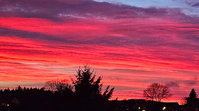Ein spektakulärer Sonnenuntergang mit intensiv leuchtenden Rottönen färbt den Himmel über einer dunklen Silhouette aus Bäumen und Häusern – dramatische Abendstimmung über Schleiz in Thüringen.