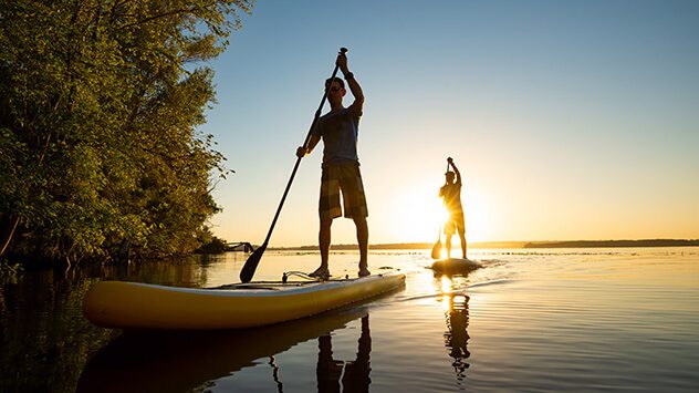 Stand-up-Paddeling bei Sonnenuntergang auf einem See (c) Sanchik/Shutterstock.com