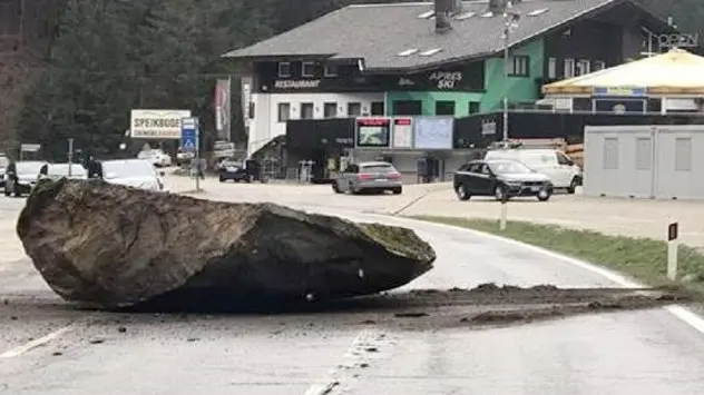 Ein riesiger Felsbrocken rollt den Berg hinunter und bleibt mitten auf der Straße stehen.