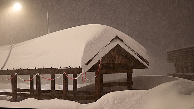 Дървено укритие, покрито със сняг по време на силен снеговалеж през нощта. Дебел слой сняг под улично осветление.