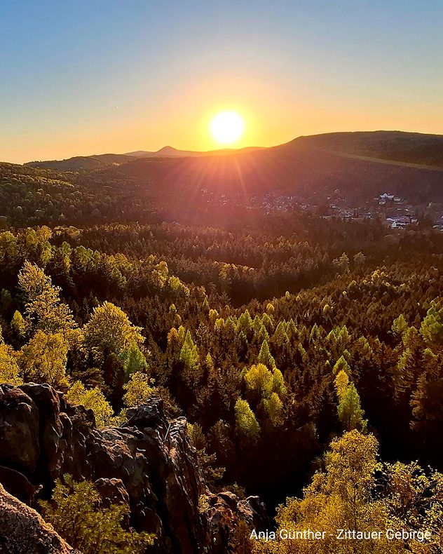 Warmes Abendlicht scheint über Wälder und Felsen im Zittauer Gebirge.