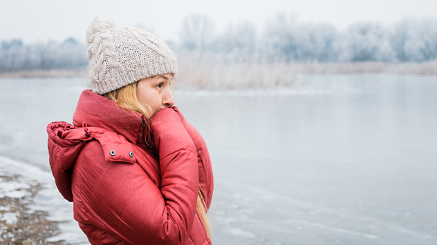 Eine frierende Frau in Winterkleidung am Wasser