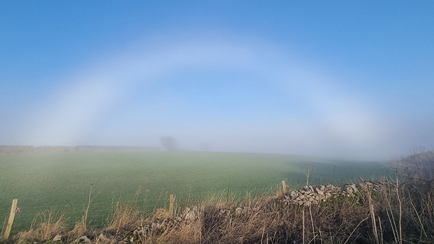 "Fogbow" pictured over a green field under blue skies in the Peak District.