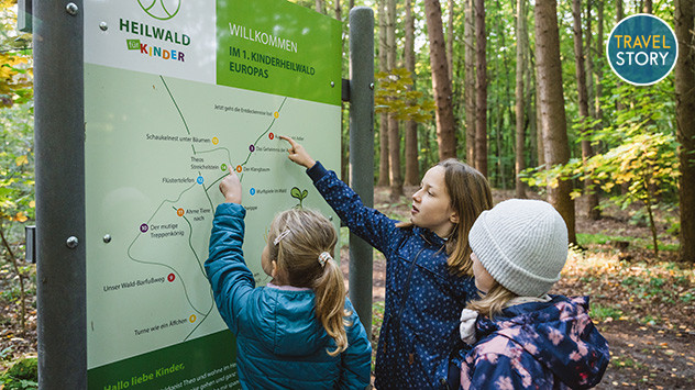 Drei Kinder schauen sich den Wegplan des Kinderheilwaldes genauer an.
