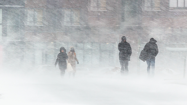 Mehrere Personen gehen bei starkem Schneetreiben und Sturm durch eine Stadtstraße, schlechte Sicht durch verwehten Schnee.