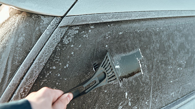 Sicher Autofahren in Herbst und Winter Ein Autofahrer kratzt die Scheibe frei.