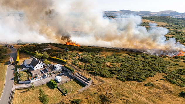 Wildfire burns in field behind home in the countryside.
