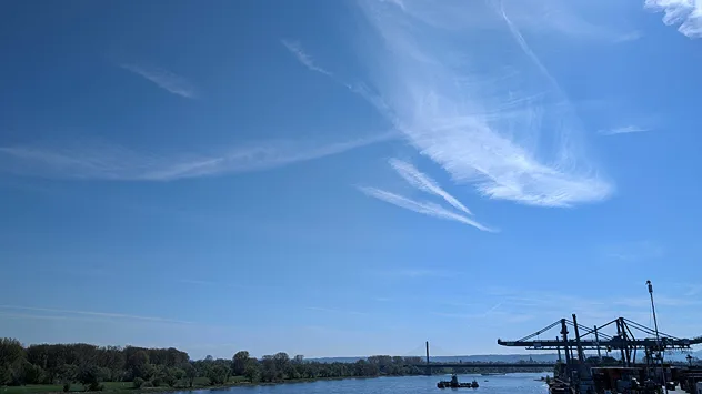 Flusslandschaft mit Hafenanlagen unter blauem Himmel mit dünnen Schleierwolken.