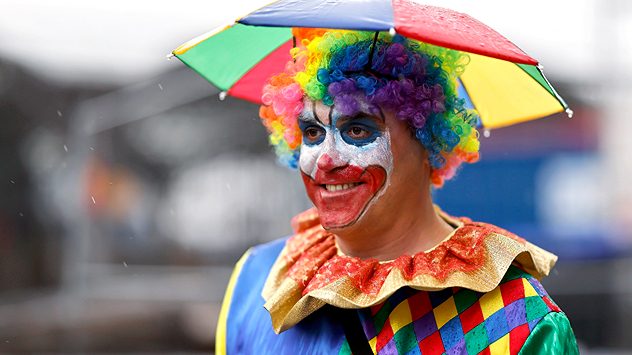 Ein Clown mit buntem Regenschirm. (c) picture alliance / Panama Pictures | Christoph Hardt