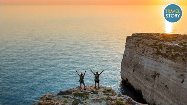 Zwei Wanderer auf einem Felsen blicken bei Sonnenuntergang aufs Meer.