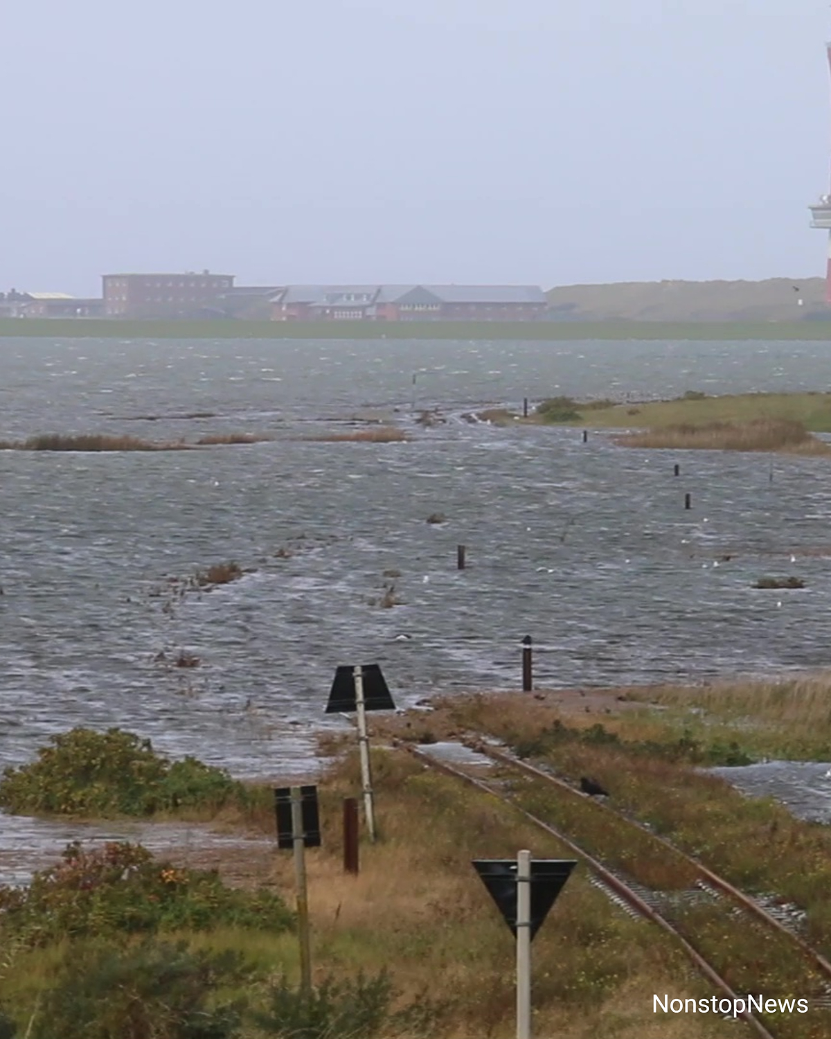 Überflutete Bahnstrecke auf Wangerooge, das Meerwasser steht bis über die Gleise, im Hintergrund Gebäude und ein Leuchtturm.