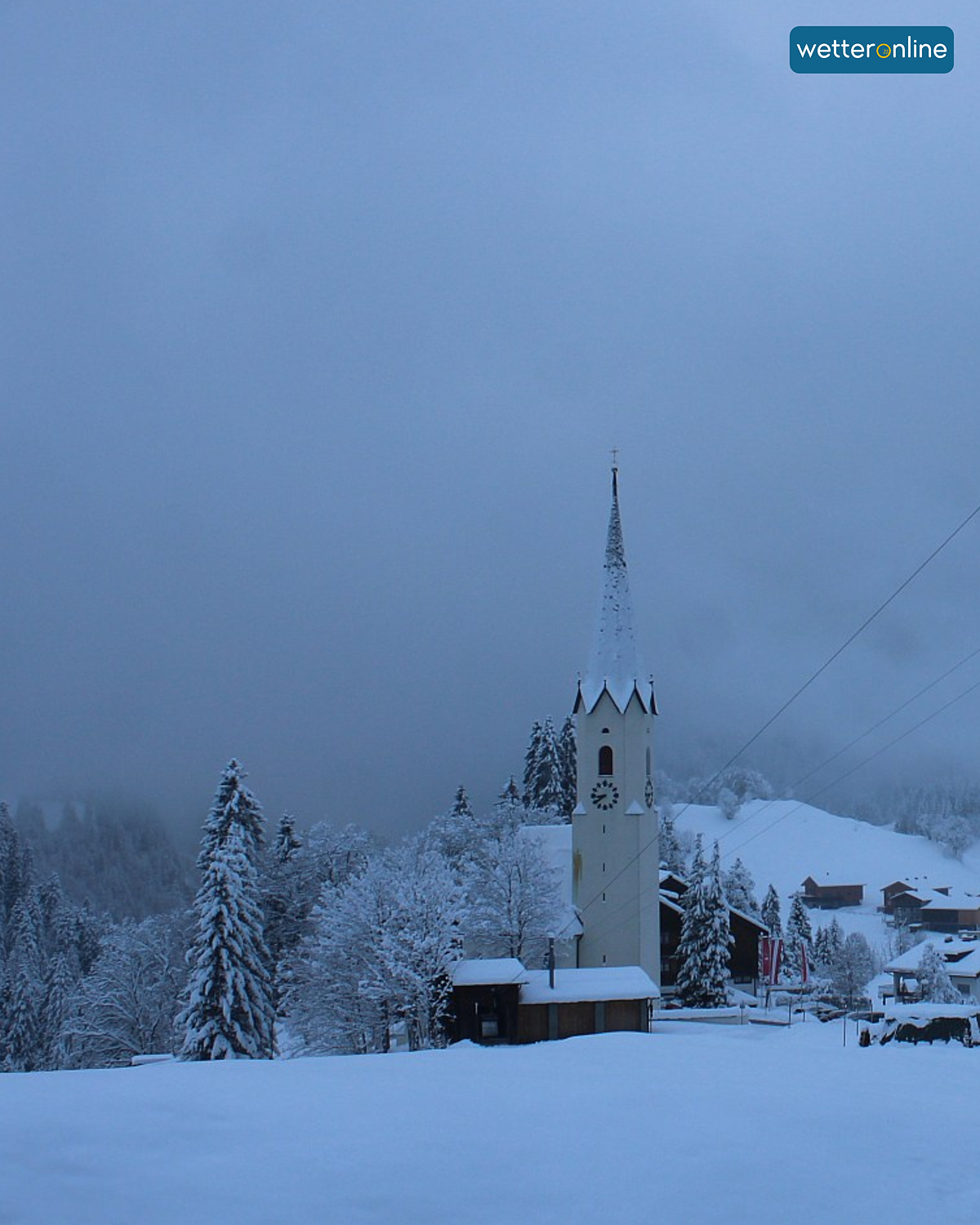 Verschneite Kirche in nebliger Winterlandschaft mit Häusern und Bäumen. Ruhige Szenerie im dichten Neuschnee.