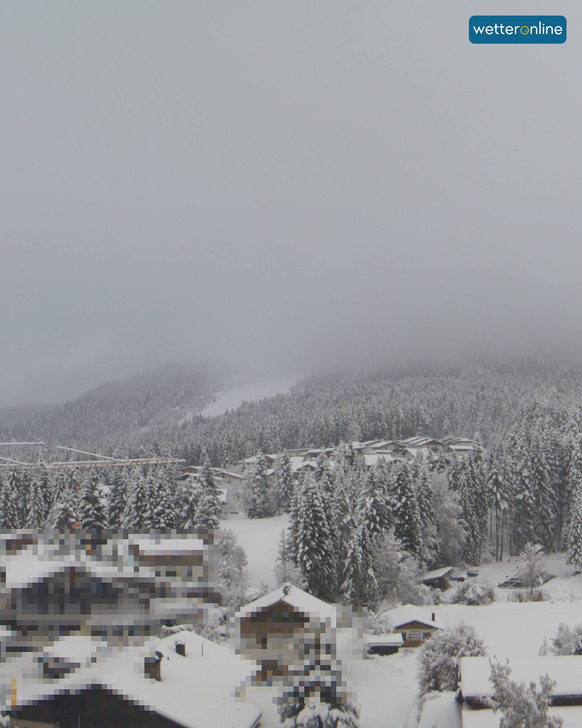 Verschneites Alpendorf mit dichtem Nebel über Wald und Hängen. Winterliche, ruhige Landschaft.