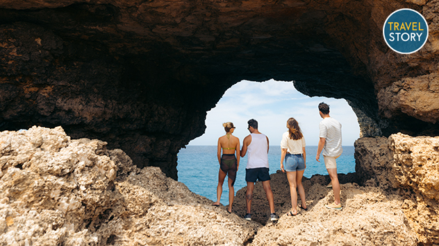 © dreambeachmedia Vier Personen blicken durch ein Felsloch aufs Meer.