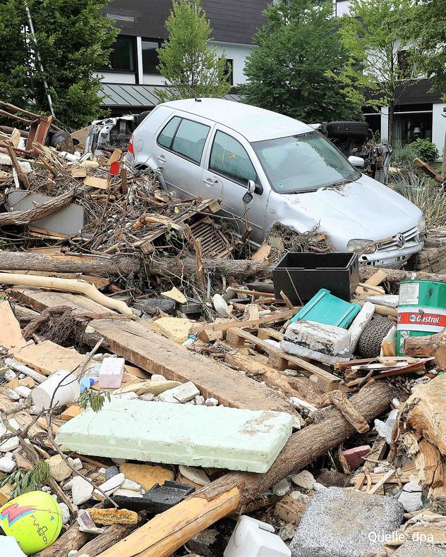 Ein Auto steckt nach der Flut zwischen Holz, Ästen und Schutt vor Wohnhäusern.