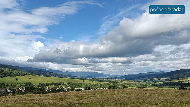 Krajina s poľom, dedinou a oblačnou oblohou.