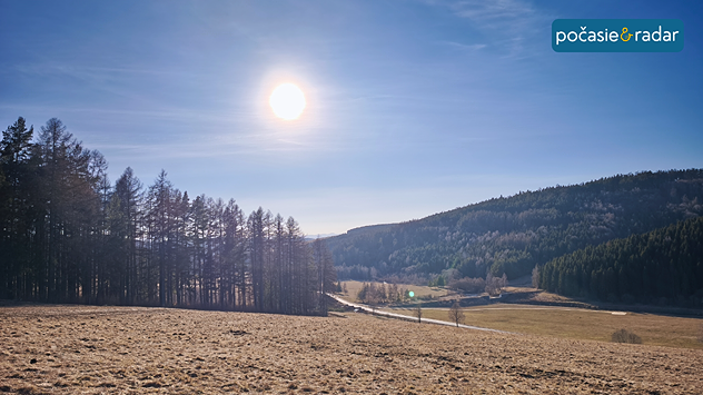 Slnečný deň nad horskou dolinou s lúkami a lesmi