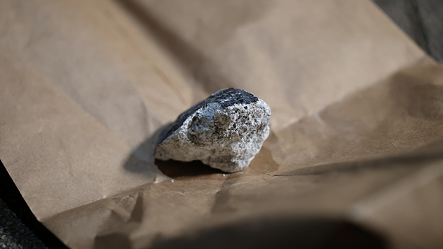 Small meteorite with dark crust on brown paper. Close-up of an irregularly shaped rock.