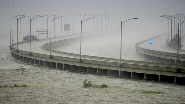 A long bridge stands in the storm, water lashes against the pillars, visibility is severely restricted by rain and spray.