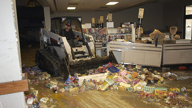 A man clears away food debris in a flooded supermarket with a small excavator.
