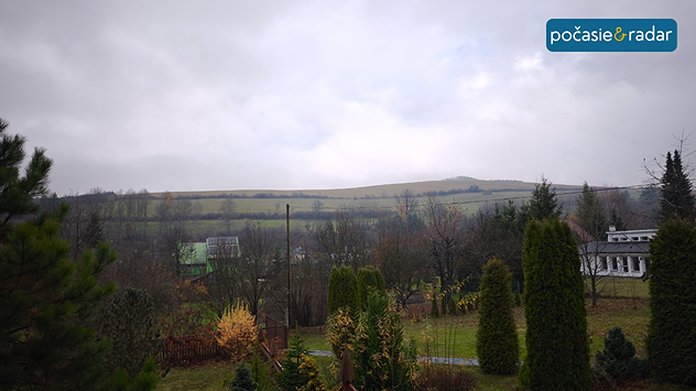 Snímka zobrazujúca prírodu - kopce, záhradu, stromy a budovy v sychravom jesennom počasí.