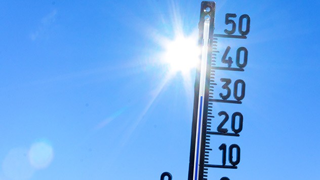 Thermometer vor blauem Himmel mit Sonne